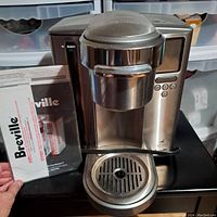 Front view of stainless steel Breville coffee maker with user manual propped beside