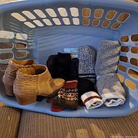 Blue plastic laundry basket holding a pair of women’s tan suede ankle boots and four pairs of socks arranged neatly inside.