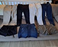 Full view of eight items including pants and shorts laid on couch showing colors and styles