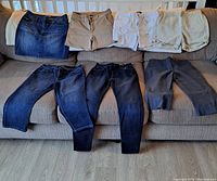 Eight women's size 8/9 bottoms displayed on couch, including denim jeans, skirt, shorts and capris in various colors.