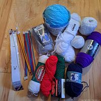 Photo showing a variety of yarn skeins in different colors plus bundled colored aluminum knitting needles and packaged knitting needles.
