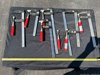 7 metal wood clamps laid out on a black cloth, showing red handles and metal bars of varying lengths