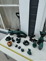 Photo showing entire collection of glazed pottery figures including dolphin, multiple ducks, cat, fox and ceramic apple on a white table.