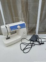 White Brother LS-2125 sewing machine with blue label panel and foot pedal with attached cord, placed on a white surface near a window.