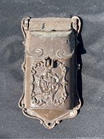 Front view of cast iron mailbox showing ornate floral embossed design and hinged top flap.