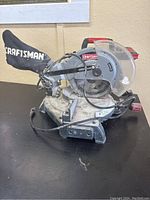Front and side view of Craftsman mitre saw showing blade, dust collector bag and base.