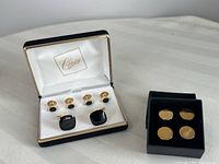 Two sets of gold tone cufflinks with black accents displayed in velvet boxes with satin interiors labeled 'Classy'. One set has larger square black stones with matching small black button cufflinks; the other set has oval black stone cufflinks with matching black button cufflinks.