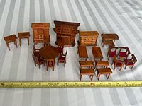 Overview of the full dollhouse dining room furniture set on a striped surface with measuring tape showing scale; includes multiple chairs, tables, and cabinets.