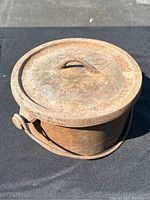 The Dutch oven with lid on, showing the heavily rusted top and curved handle on the lid.
