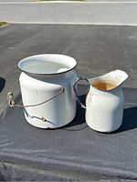 Photo of larger pale and smaller jug placed together on a black surface outdoors, showing general shape and handles.