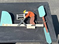 Full view of the folk art whirligig showing the carpenter figure, workbench, horizontal wooden plank, and spinning blades.