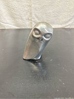 Front view of the silver metal owl sculpture showing stylized eyes and rounded form on a flat surface.