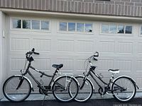 Two step-through Giant bikes parked side by side in front of a garage door, showing both frames, fenders, racks, and bags.