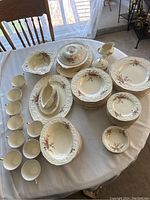 Full view of the arrangement on dining table showing multiple stacks of plates, bowls, cups, saucers, a covered serving dish, a gravy boat, and a small covered sugar bowl.