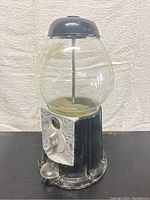 Front angle view showing metal coin slot, black metal base, and clear glass globe.