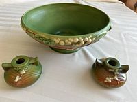 Top view of green Roseville fruit bowl with two matching candlesticks on a white tablecloth, showing interior and exterior fruit and leaf design.