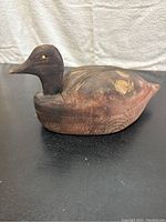 Side view of wooden duck decoy showing dark head, yellow eyes, and worn painted body.
