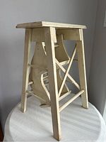 Another side view of the wooden step stool showing the standing form and legs with cross supports.