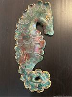 Single image showing glazed ceramic seahorse wall art with worn surface and a curled tail detail.