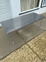 Full view of stainless steel prep table standing outdoors on concrete showing overall structure, legs, and surface condition.