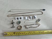 All sterling silver jewelry in the lot laid out with ruler for scale, including rings, bracelets, earrings, and chains