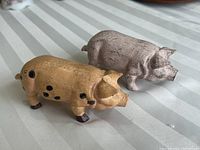 Two cast iron pig figurines side by side on a striped cloth surface showing overall condition and details