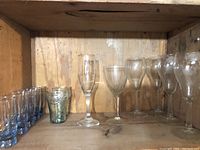 Photo of small blue drinking glasses, textured Coca-Cola glasses, and clear wine glasses including champagne flutes