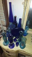 Collection of blue glass bottles and vases arranged on a wooden dresser with a mirror behind