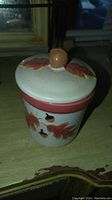 Front view of the ceramic jar with lid showing the round knob handle and the painted autumn leaves and acorns.