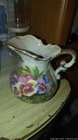 Side view of ceramic pitcher showing floral artwork and gold accents on rim and handle