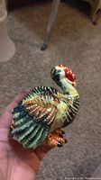 View of ceramic turkey pepper shaker held in hand showing colorful paint and detailed feathers.