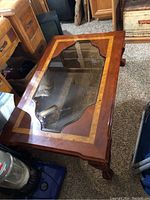 Top and angled view of wood coffee table showing decorative glass insert and carved legs