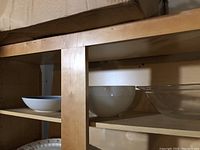 View of wooden shelves holding white ceramic mixing bowls and plates