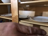 Plain white ceramic plates stacked on wooden shelves.