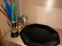 Black octagonal plate and decorative ceramic turkey figurine, shown on shelf