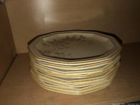 Stack of eight octagonal plates with floral pattern and yellow trim.