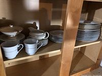 Photo of shelf with stacked dishes, cups, and serving pieces.