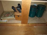 Wooden knife block containing knives, decorative tin box, small unidentified item on wood shelf
