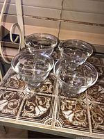 Four clear glass ice cream cups displayed on a patterned surface, showing the overall set and design.