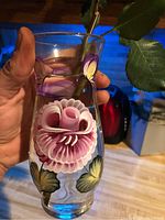 Clear glass vase held in hand showing detailed hand-painted pink and purple flower and green leaves design.