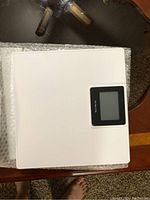 Digital bathroom scale with white top surface and black LCD display, bubble wrapped.