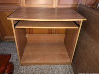 Front view of the small wooden computer desk, showing pull-out keyboard tray and open bottom shelf space.