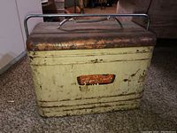 Front view of the vintage metal cooler showing rust on lid, cream body with age wear and the 'Thermo Chest' label
