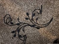 Two black wrought iron wall decor pieces shown on carpeted floor with curved and leaf designs.