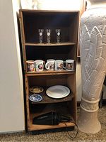 Wooden shelf with three shelves shown with glassware, mugs, plates, and a hair dryer for context, which are not included.