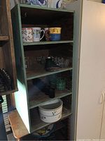 Full view of the green painted wooden shelf unit containing four shelves, showing natural wood interior and some wear marks.