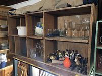 Frontal view of the wooden shelf with some glassware and decorative items on or around, showing internal compartments and wear on wood.