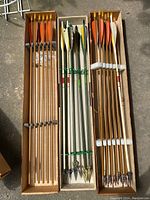 Top view of three boxes filled with wooden arrows of different designs showing fletching at the nock end.