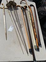 Overview of six canes and three fencing swords laid out on a table, showing full lengths and details.