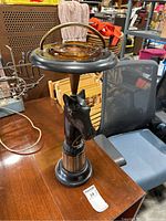 Full view of the standing ashtray showing black horse head base, circular black top with brass handle and amber glass ashtray insert.